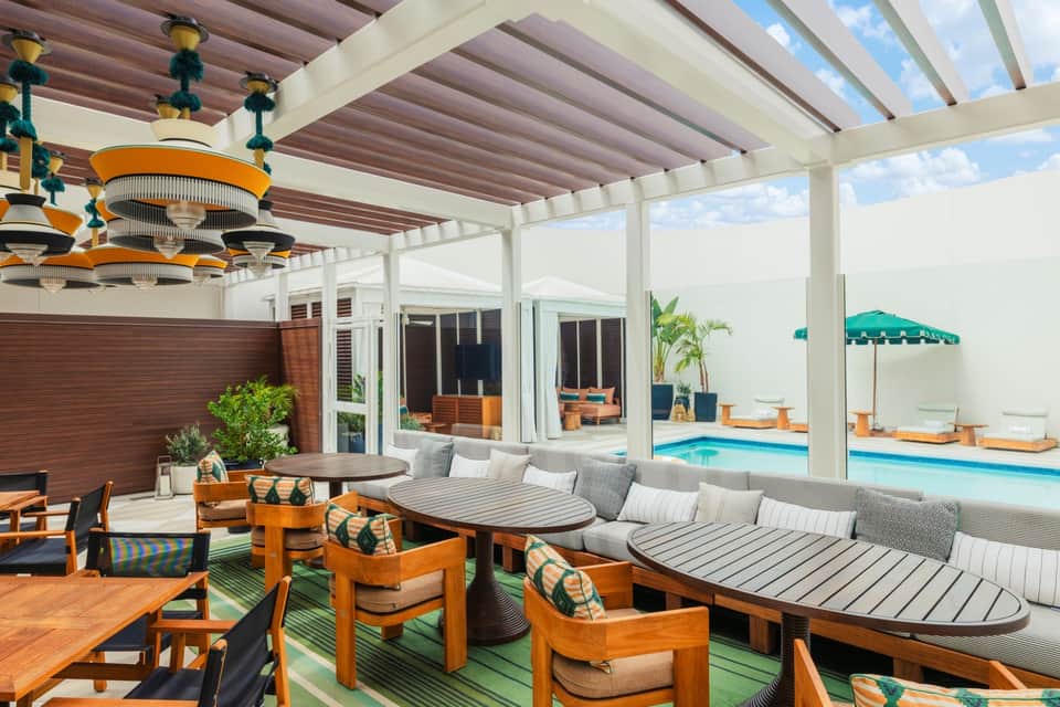 Modern lounge area with wooden chairs, gray upholstered seating, orange accents, and view of pool through open architecture