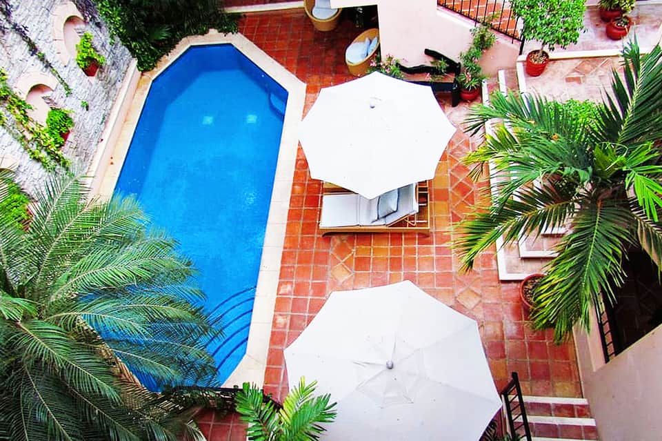Overhead view of blue rectangular pool with white umbrellas on red tile courtyard