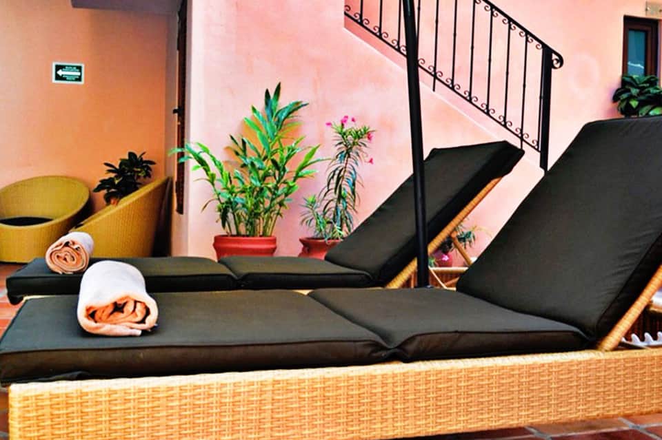 Spa relaxation area with two black loungers, potted plants, and peach-colored walls with wrought iron railing