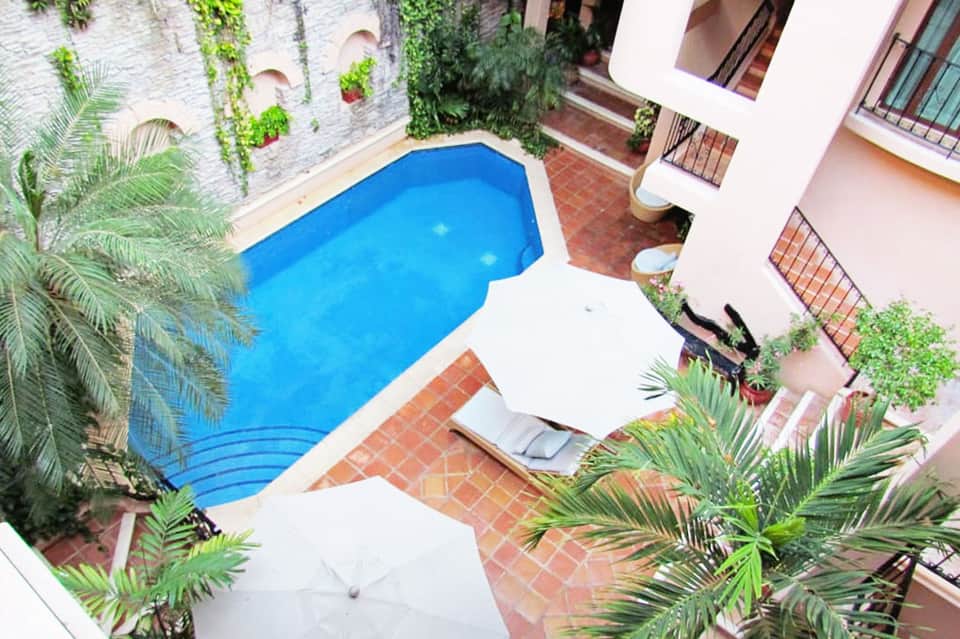 Aerial view of curved blue pool in courtyard surrounded by pink building and tropical plants