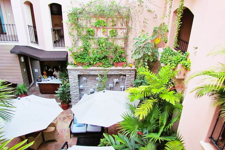 Courtyard with pink walls, ivy-covered trellis, lounge seating, and stone water feature