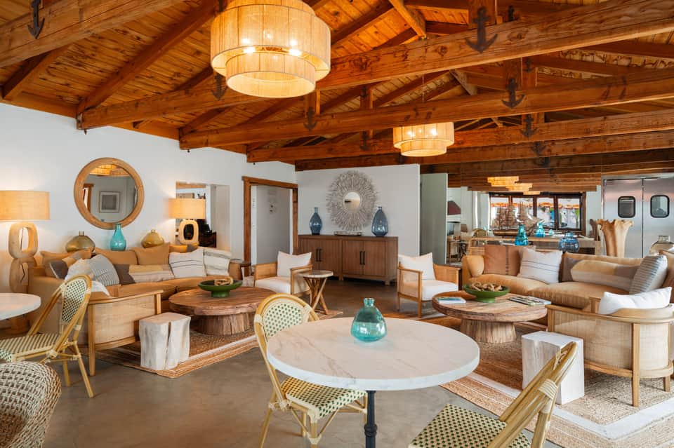 Spacious mid-century modern living room with exposed wooden beams, marble tables, rattan chairs, and turquoise accents