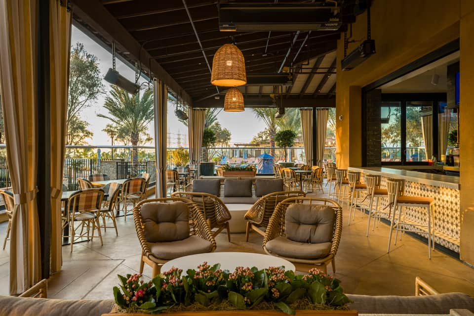 Covered outdoor lounge area with woven pendant lights, comfortable seating, and views of palm trees and waterfront