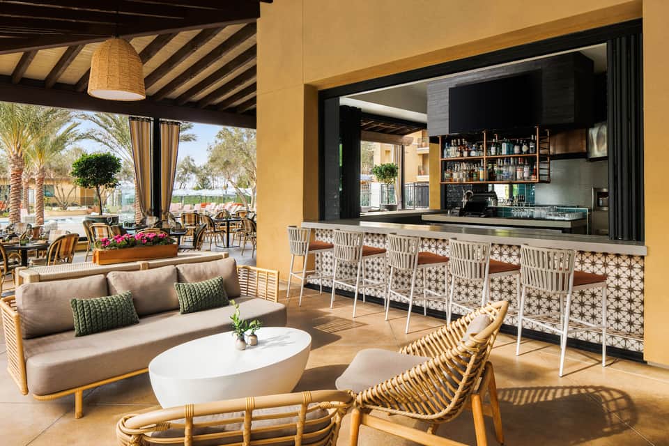 Outdoor bar and lounge with yellow walls, woven furniture, fireplace, and views of pool area beyond