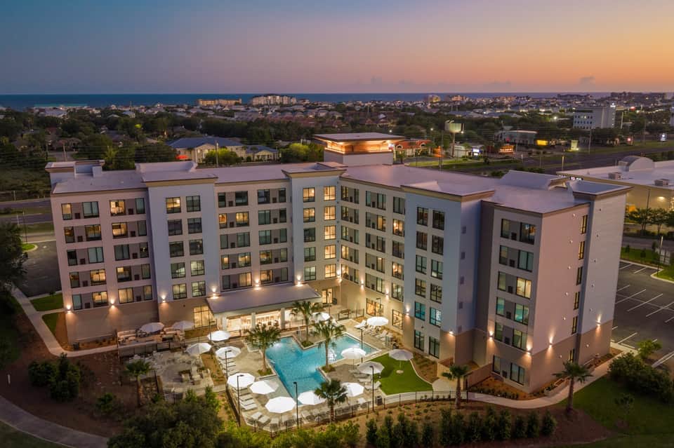 Aerial view of modern apartment complex with illuminated pool courtyard at twilight