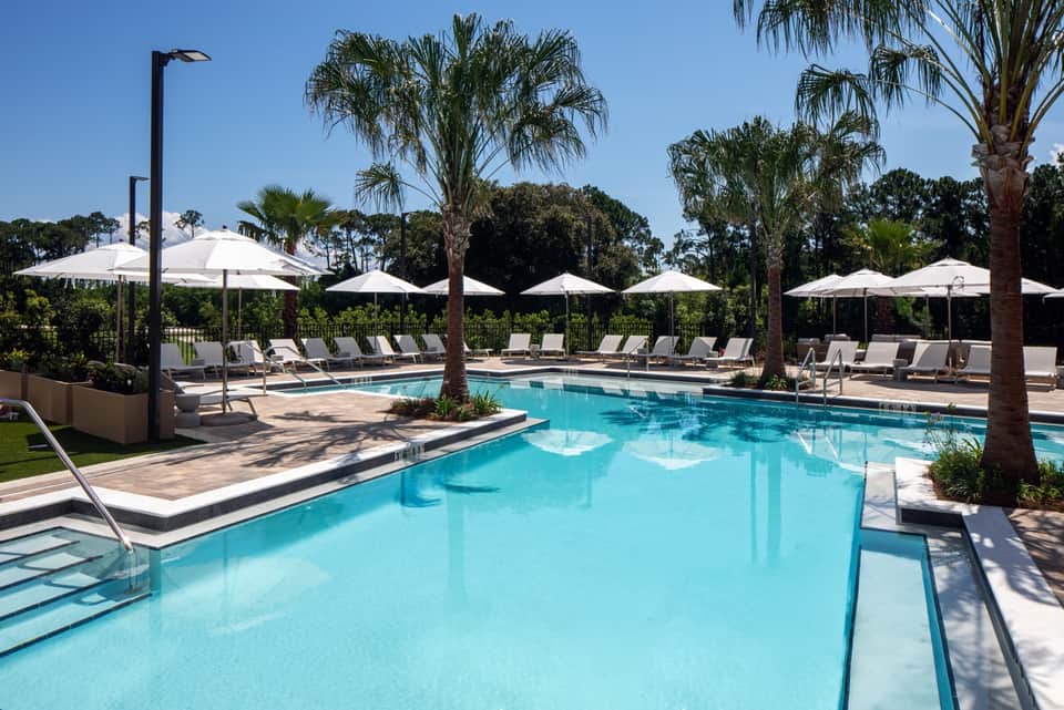Large resort pool surrounded by palm trees, white umbrellas, and lounge seating areas