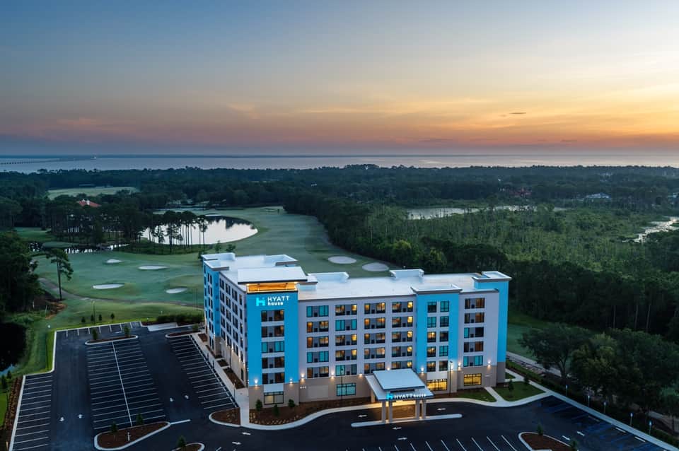 Modern Hyatt hotel overlooking golf course and waterfront at sunset with parking area