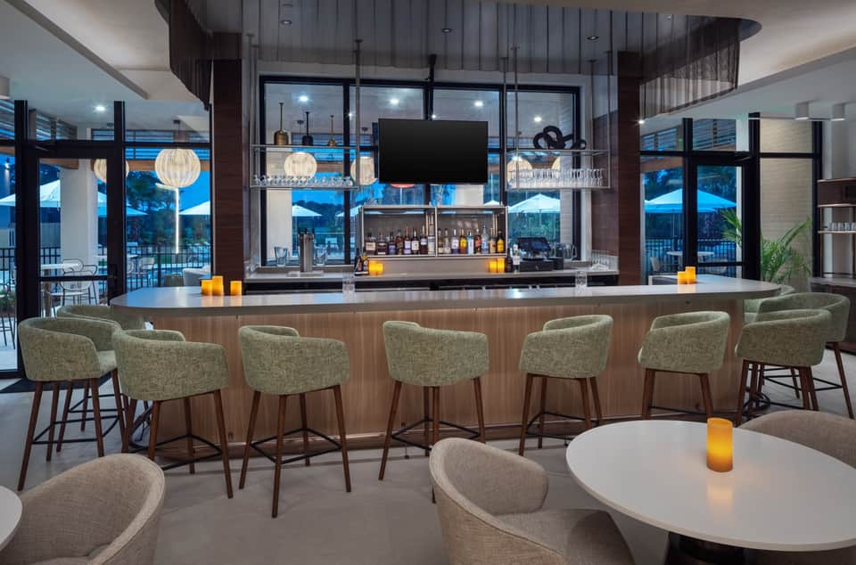 Contemporary hotel bar with modern counter seating, pendant lighting, and pool view windows
