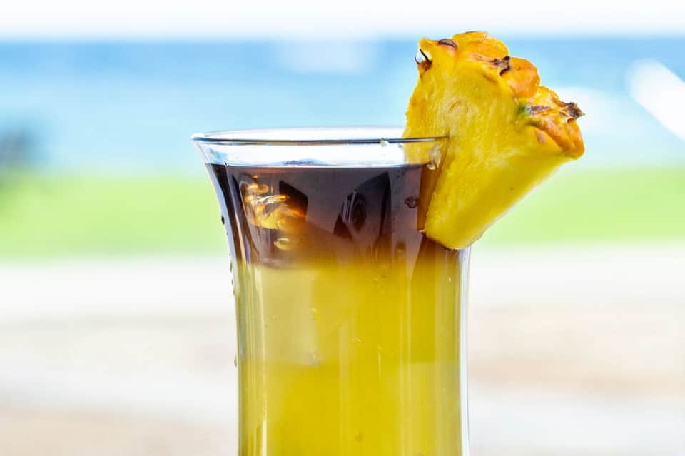 Tropical cocktail with pineapple garnish against beach and ocean backdrop