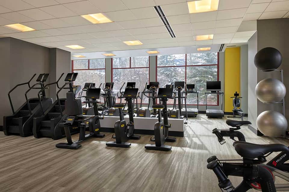 Modern fitness center with rows of stationary bikes, treadmills, exercise balls, and large windows overlooking trees