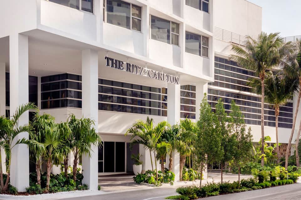 Modern white hotel building with palm trees and landscaped entrance featuring 'The Ritz Carlton' signage