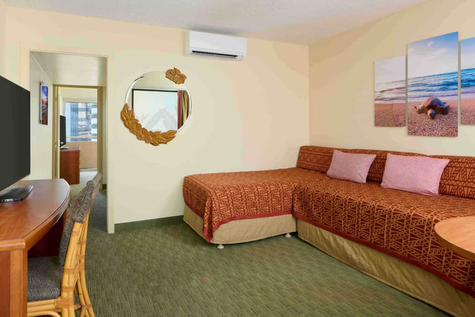 Suite with two beds, sofa, TV, and beach-themed wall art