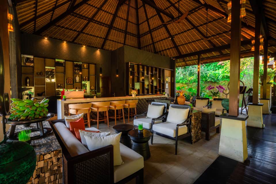 Open-air tropical resort pavilion with wooden ceiling, bar, lounge seating and lush greenery