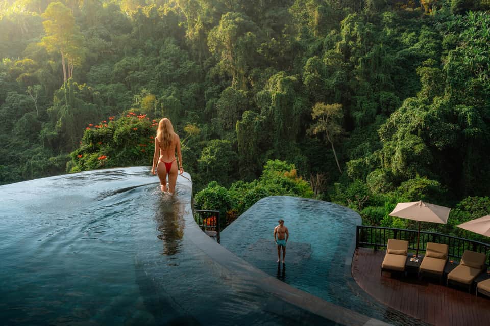 Infinity pool overlooking dense forest canopy with guests swimming at luxury jungle resort