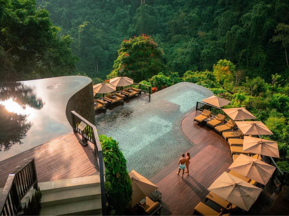 Luxury infinity pool overlooking dense tropical forest with loungers and umbrellas on wooden deck
