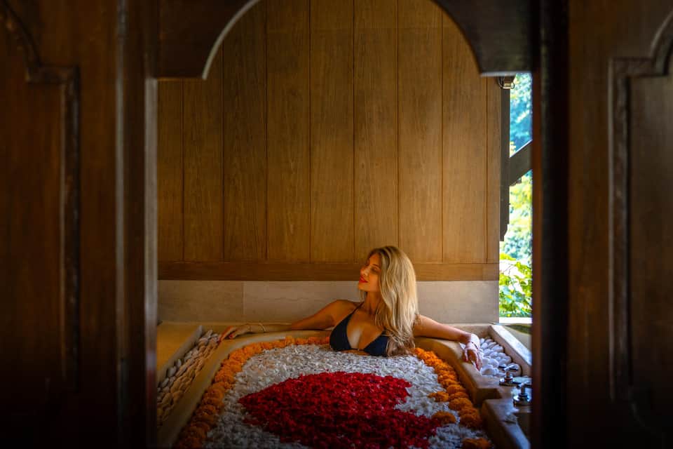 Woman in flower petal bath with red, white, and orange marigolds in wooden spa pavilion