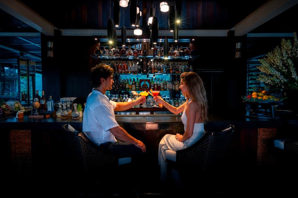 Couple toasting colorful cocktails at an upscale bar with blue ambient lighting and full liquor shelves