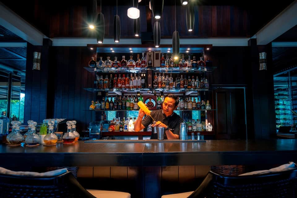 Bartender preparing a yellow cocktail behind a modern bar with illuminated bottle display