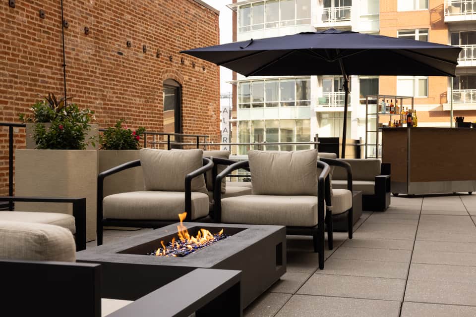 Outdoor fire pit seating area with beige cushioned chairs and black umbrella on terrace