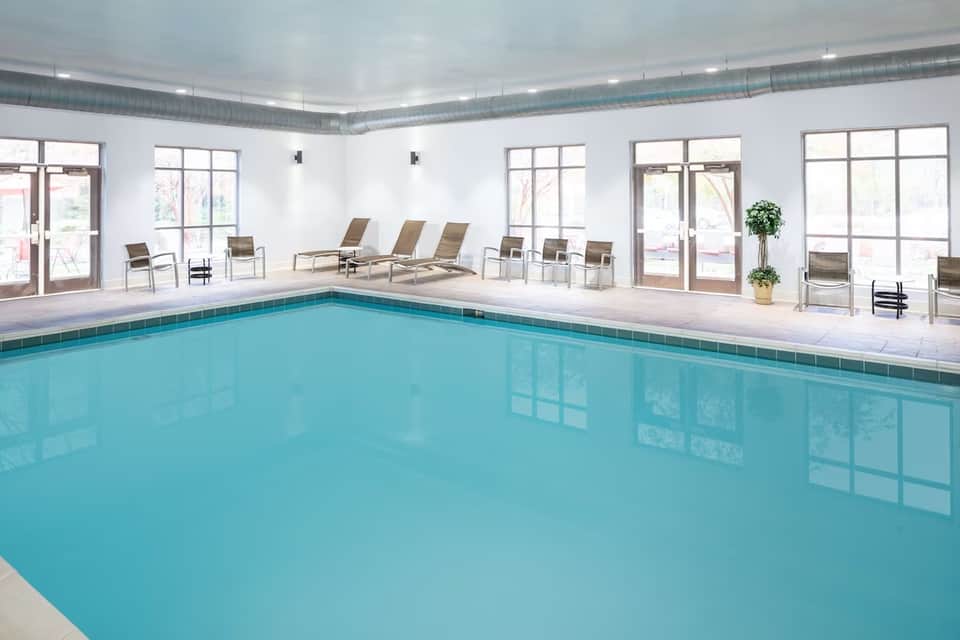 Indoor swimming pool with lounge chairs, expansive windows, and bright, clean white and blue tiled surroundings
