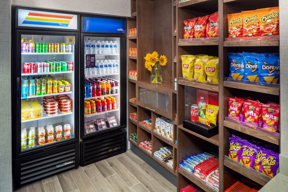 Hotel convenience market with refrigerated beverage coolers and wooden shelving stocked with snacks and drinks