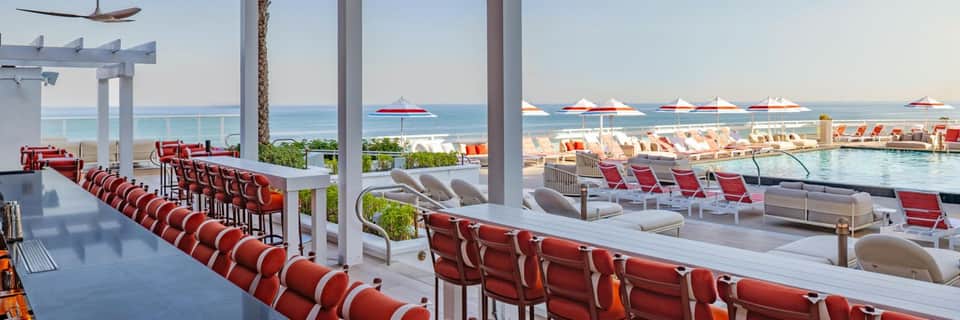 Resort poolside bar with red lounge chairs overlooking ocean and beach umbrellas