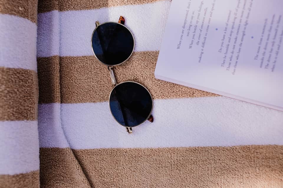 Sunglasses resting on a striped towel next to papers on a beach lounge chair