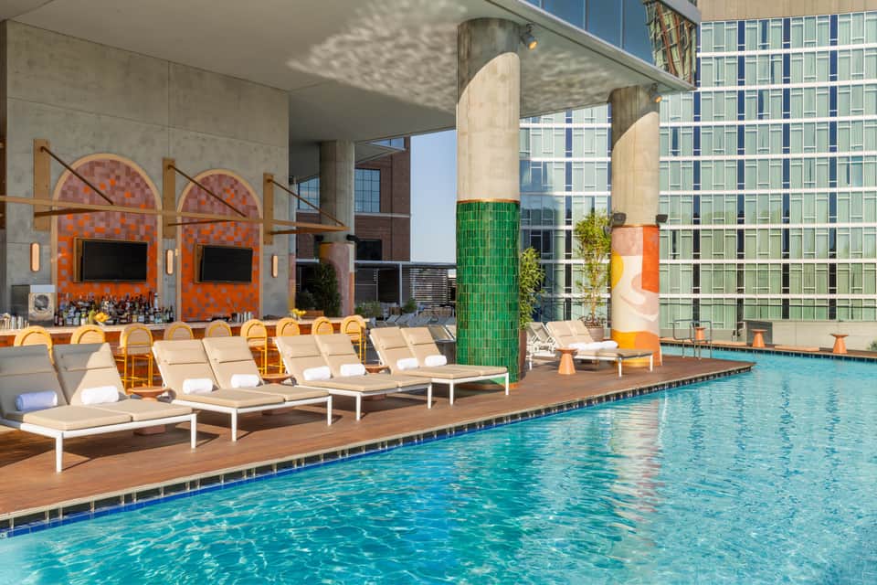 Modern rooftop pool with lounge chairs, colorful art installations, and city skyline views surrounded by tall buildings