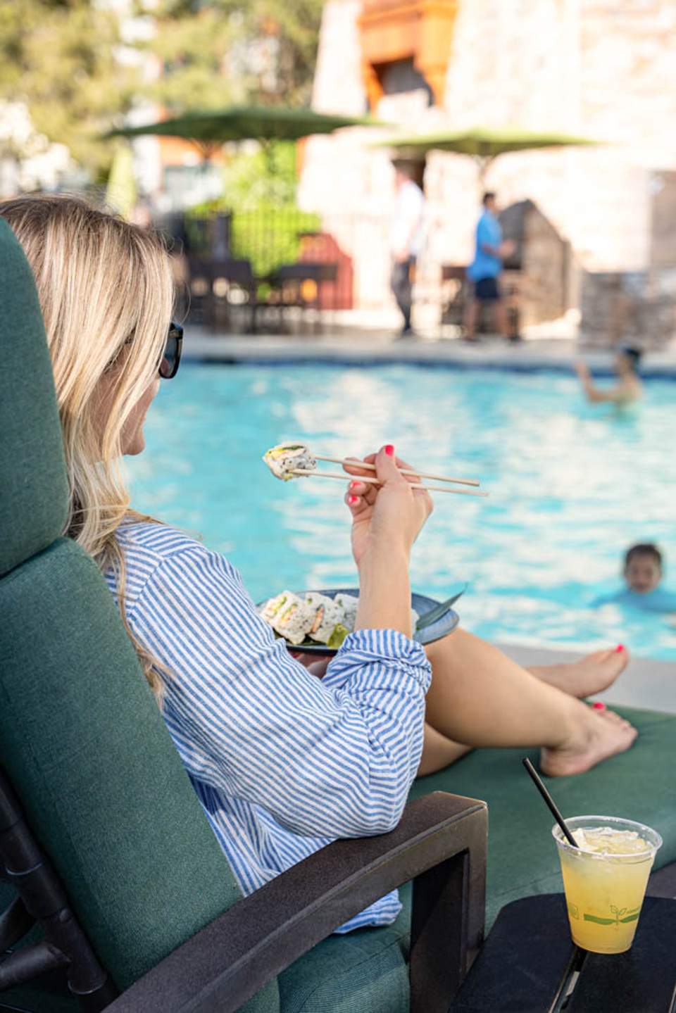 Woman poolside enjoying appetizers with a cocktail, overlooking resort pool and tropical setting