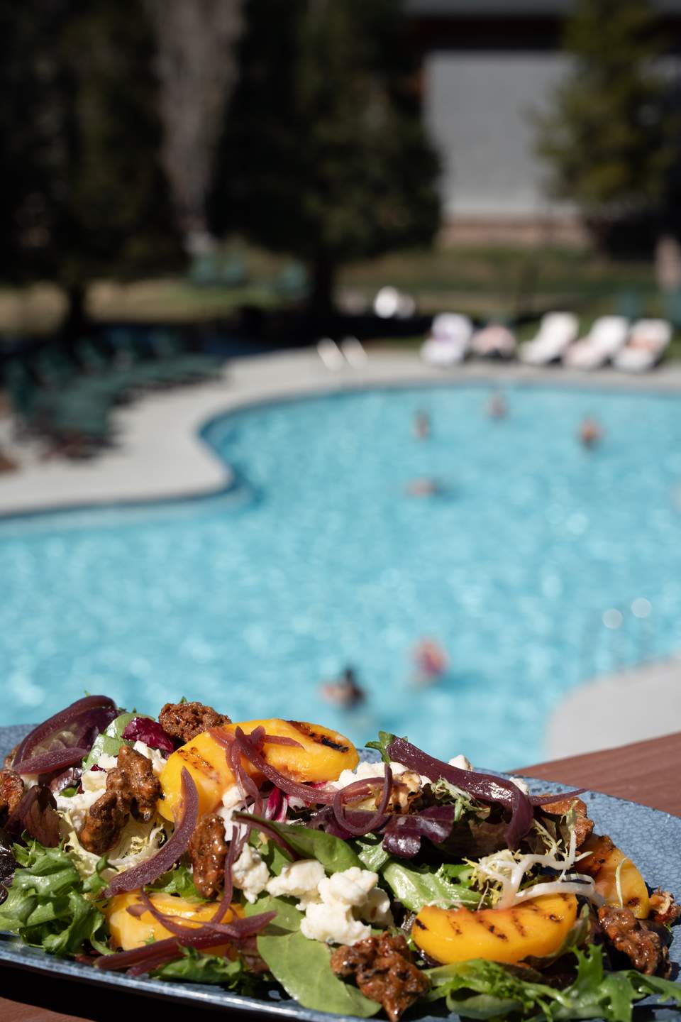 Gourmet salad with grilled peaches, beets, and goat cheese poolside at a resort with swimmers in the background