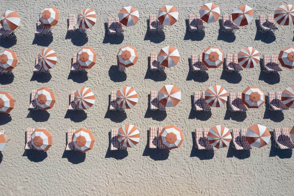 Aerial view of beach with rows of red and white striped umbrellas and sunbathers
