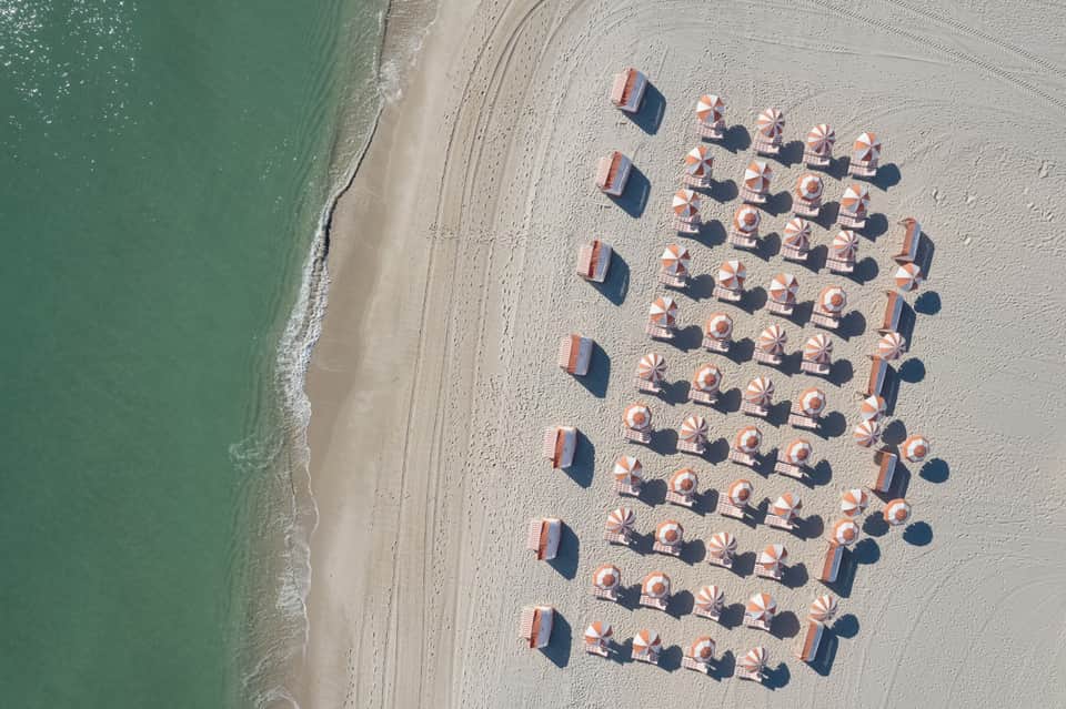 Aerial view of organized beach with red and white striped umbrellas and lounge chairs on sand