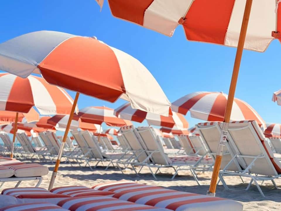 Close-up of red and white striped beach umbrellas with lounge chairs under clear blue sky