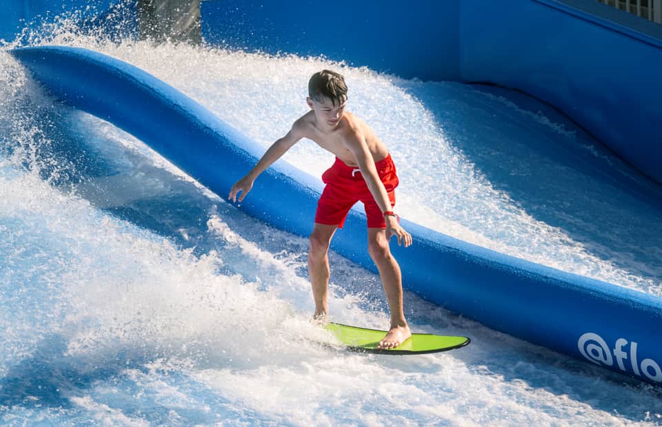 Boy surfing on a green board down a blue FlowRider artificial wave machine