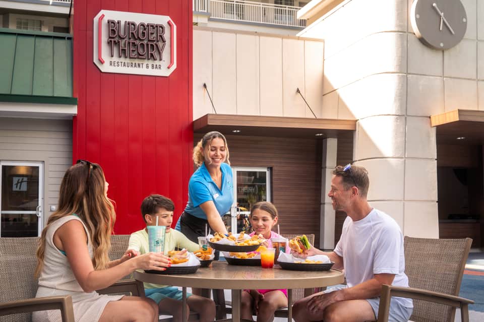 Family dining outdoors at Burger Theory restaurant on a patio with red accent wall