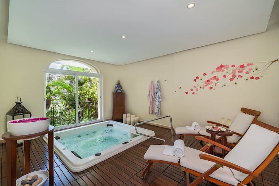 Spa relaxation area with hot tub, massage beds, flowers, and garden view through glass doors