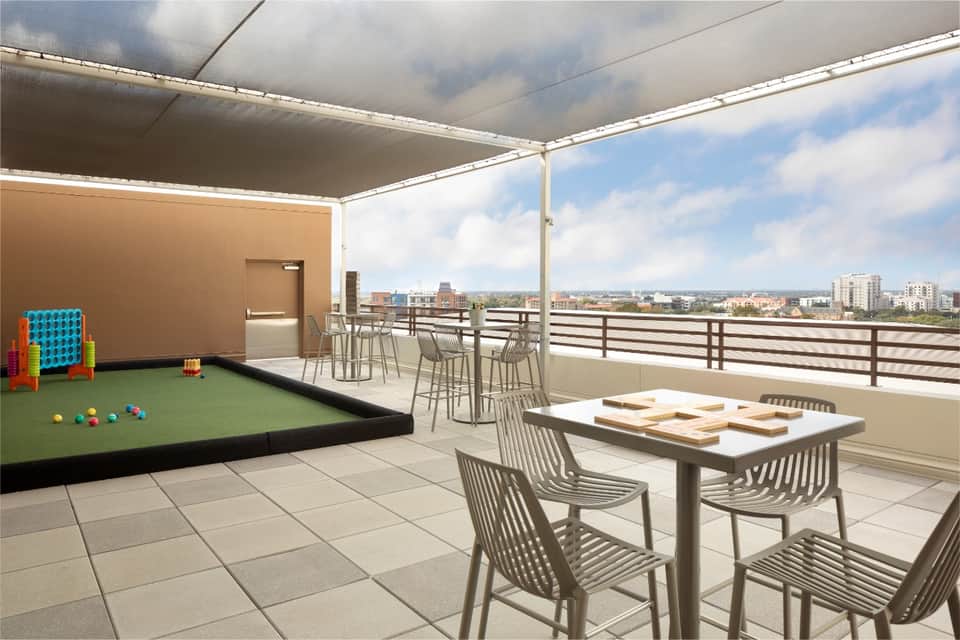 Rooftop terrace with retractable shade, dining table, mini golf area, and city views