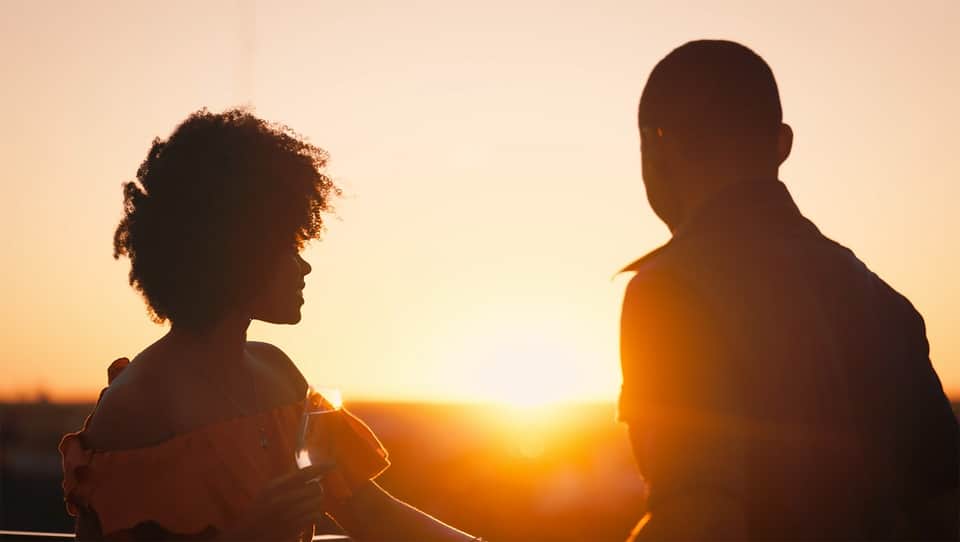 Two silhouetted figures at sunset on rooftop terrace with golden sky backdrop