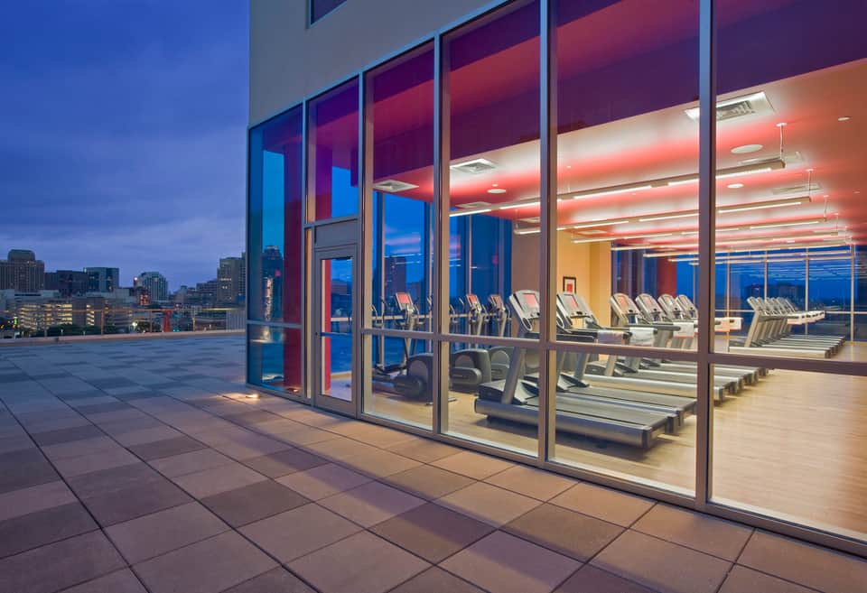 Modern gym facility with treadmills visible through floor-to-ceiling glass windows at dusk