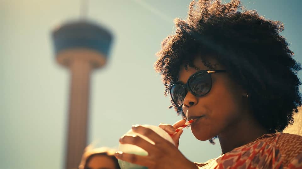Woman with curly hair and sunglasses eating snack with tower landmark blurred in background