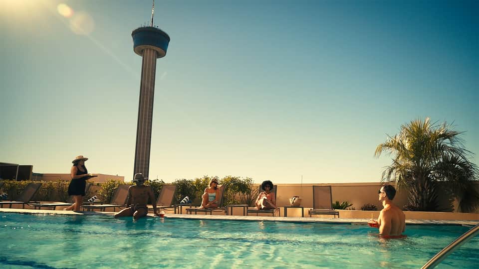 People enjoying rooftop pool with Hemisfair Tower visible under clear blue sky
