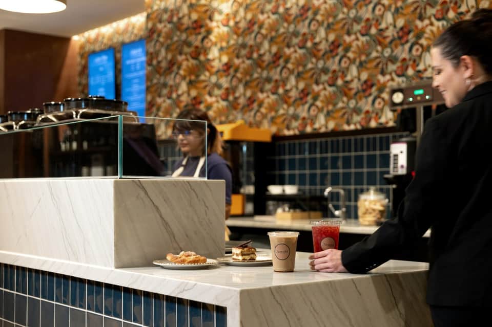 Modern café counter with staff member and colorful patterned wallpaper background