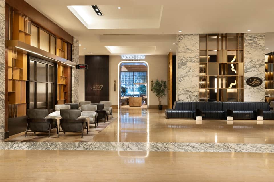 Luxury hotel lobby with marble columns, modern furniture, and Moody Bike neon sign