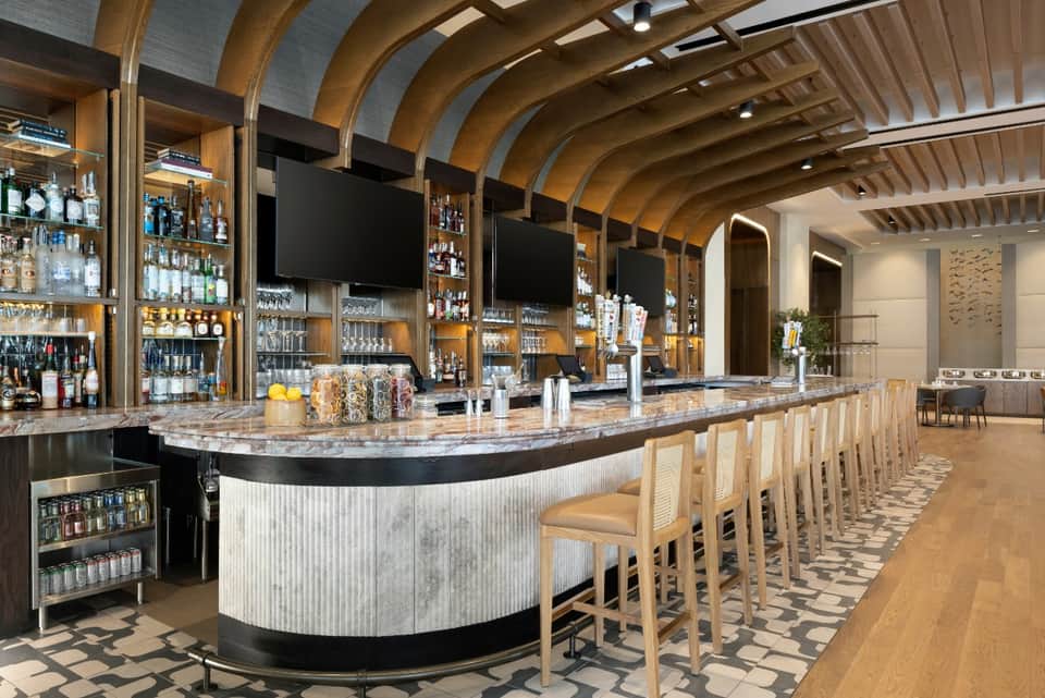 Modern bar with curved white marble counter, wooden archway ceiling, and extensive liquor shelving
