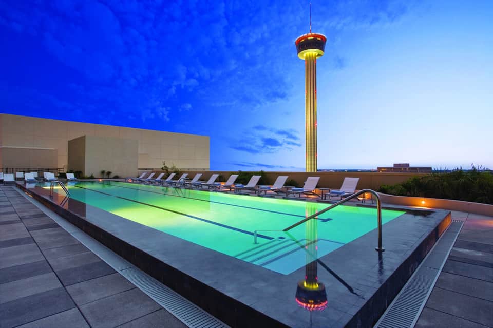 Illuminated rooftop pool at dusk with the Tower of the Americas visible in San Antonio skyline