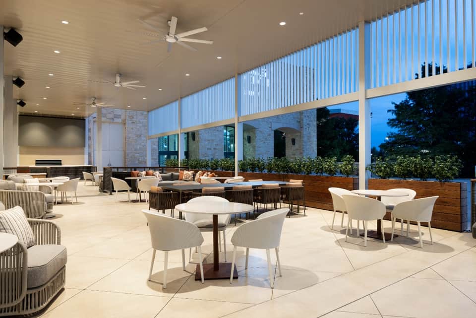 Modern outdoor terrace with comfortable seating, tables, white pillars, and evening blue light ambiance