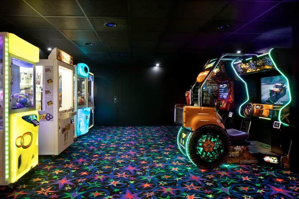 Colorful game room with arcade racing game and claw machines under vibrant neon and star-patterned flooring