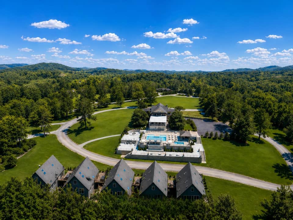 Aerial view of resort property with pools, guest cottages, and forested landscape