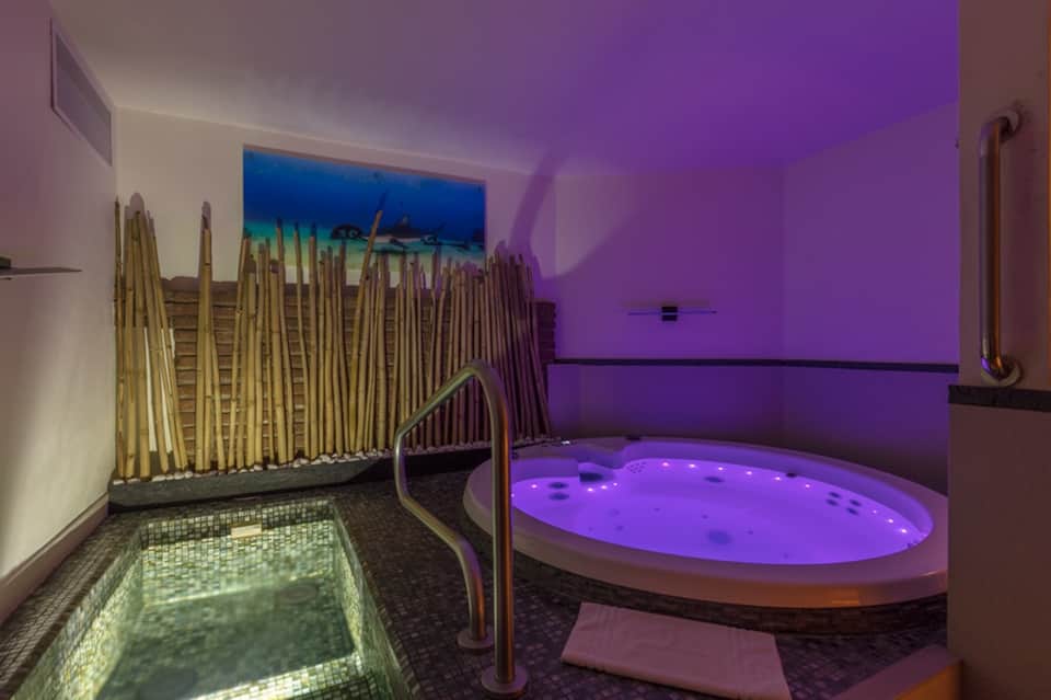 Spa relaxation area with purple-lit jacuzzi, bamboo accents, and decorative pool featuring underwater lighting