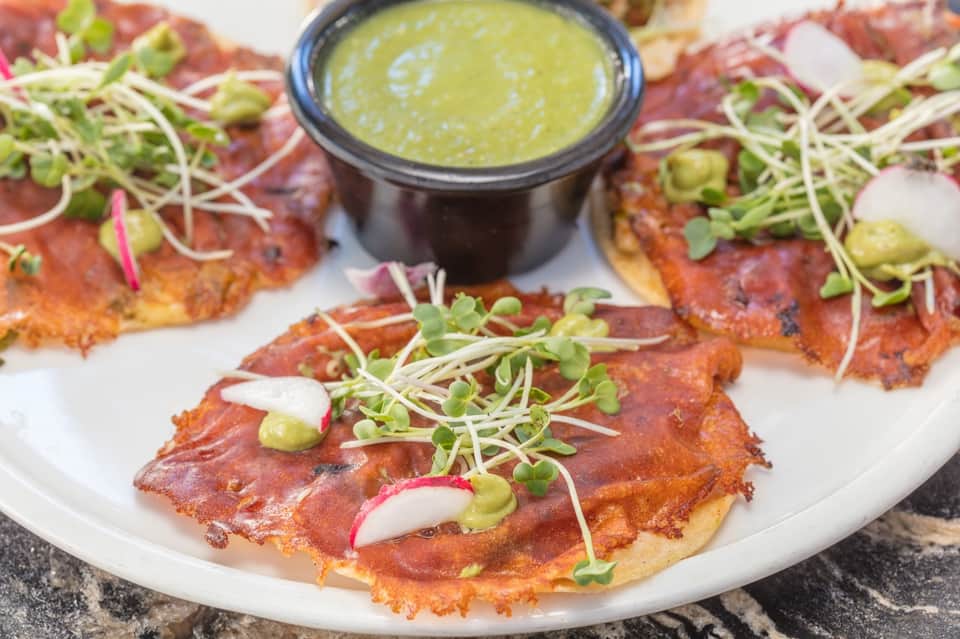 Gourmet appetizer plating with crispy base, cured meat, microgreens, radish, and herb oil sauce